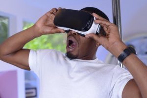 Black man in bedroom wearing Gear VR hedset, looking shocked at what he sees